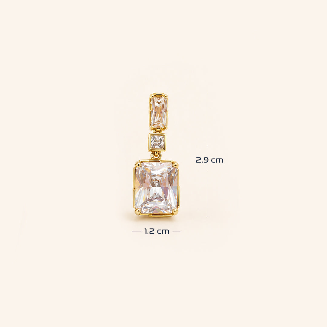 A pair of gold drop earrings featuring rectangular clear crystals in gold bezel settings, accented with small round clear stones, shown on a light cream background with size.