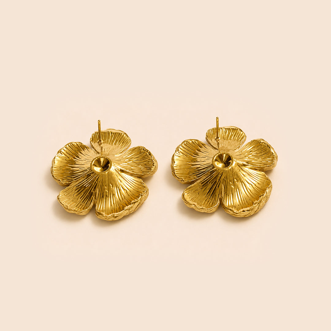 A pair of textured gold flower stud earrings on a solid pale beige background.