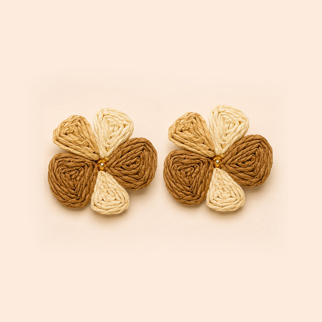 A pair of handmade braided flower-shaped earrings in shades of brown, tan, and cream, arranged side-by-side on a solid pale peach background.