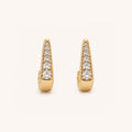 A pair of gold huggie  earrings, each adorned with a vertical row of round-cut clear gemstones, set against a clean off-white background.