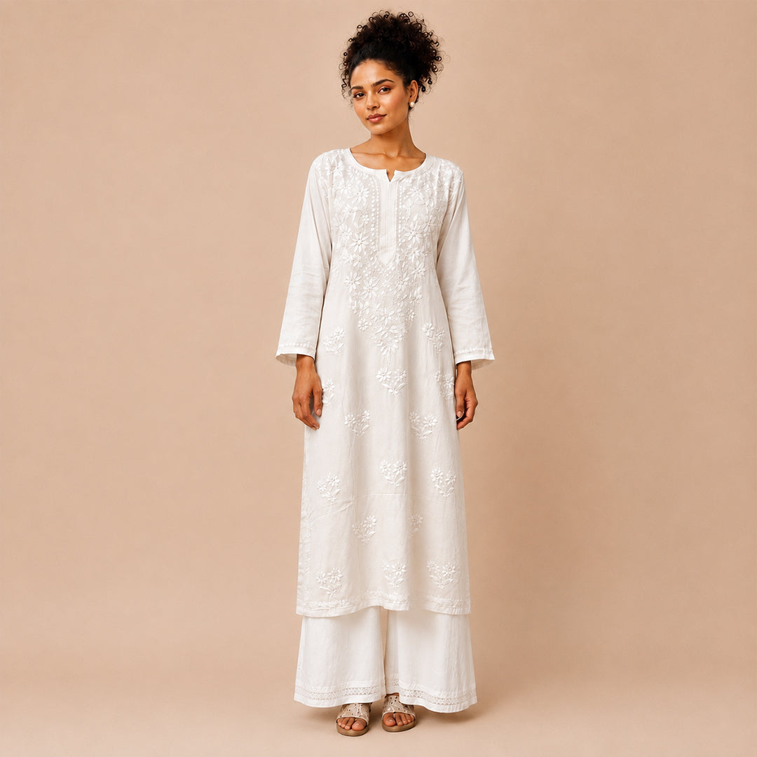 A woman modeling a white embroidered kurta with matching white palazzo pants against a solid beige studio background.