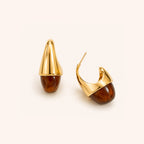 A pair of gold and Tortoshell drop earrings on a clean, light beige background. One earring is shown from the front, displaying its polished gold conical top and brown tortoshell drop, while the other is shown from the side, displaying the gold hook and the tortoshell drop.