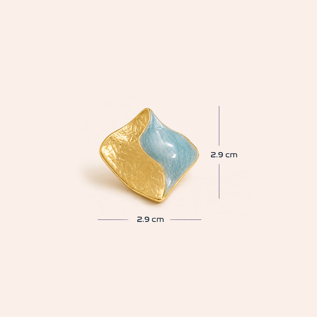 An organic-shaped gold and light blue earrings with textured gold surfaces and smooth blue inlays, displayed on a warm off-white background with size.