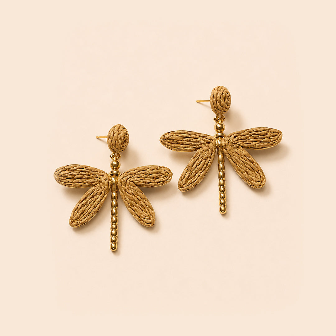 A pair of gold dragonfly earrings with textured woven wings and beaded stems, displayed on a light beige background.