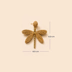 A single dragonfly-shaped woven earring in a warm tan/gold tone on a plain beige background, with measurement lines and text indicating 6.0 cm width and 6.