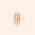 A gold ring decorated with pink enamel cherry  flowers and small clear stones, shown on a light beige background with dimension lines indicating 1.0 cm width and 2.