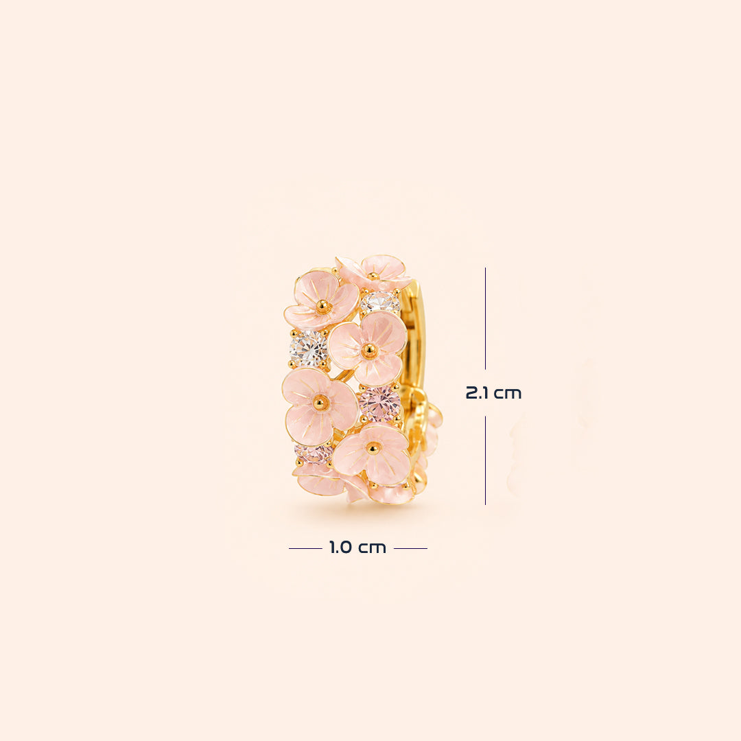 A gold ring decorated with pink enamel cherry  flowers and small clear stones, shown on a light beige background with dimension lines indicating 1.0 cm width and 2.