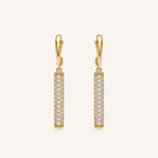 A pair of gold leverback drop earrings with vertical pavé columns of clear stones, shown on a clean off-white background.