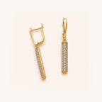A pair of gold drop earrings with pavé-set clear stones on a clean, light cream background.