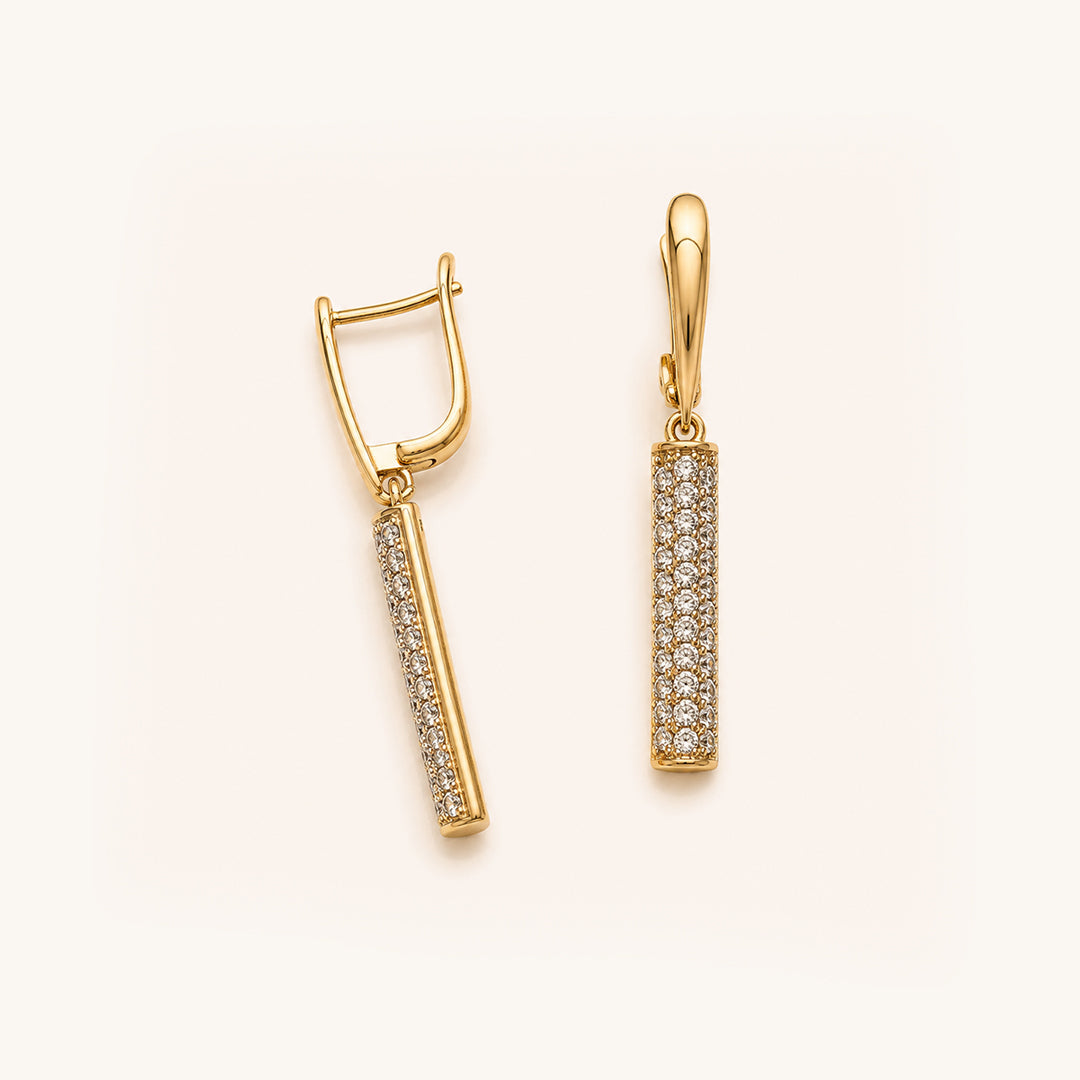 A pair of gold drop earrings with pavé-set clear stones on a clean, light cream background.