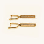 A pair of gold-toned rectangular bar earrings with a textured pavé-style center and a curved openwork hinged back, shown on a clean off-white background.