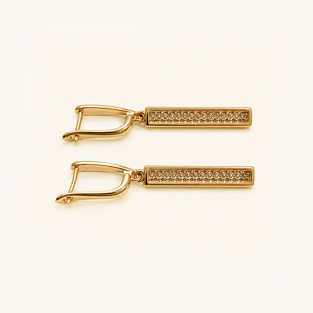 A pair of gold-toned rectangular bar earrings with a textured pavé-style center and a curved openwork hinged back, shown on a clean off-white background.