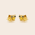 A pair of gold owl stud earrings with dark green enamel eyes, white enamel beaks, and small white flower charms, displayed on a light beige background.