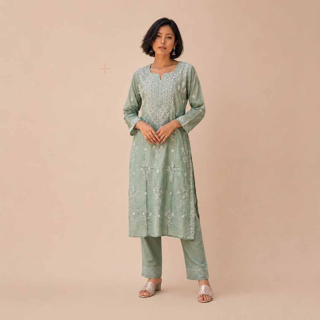 A woman modeling a sage green embroidered kurta set with matching pants against a solid beige studio background.