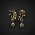 A pair of ornate Indian Jhumka earrings in gold-toned metal with red, green, and turquoise enamel details, set against a dark textured background.