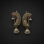 A pair of ornate Indian Jhumka earrings in gold-toned metal with red, green, and turquoise enamel details, set against a dark textured background.