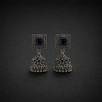 A pair of traditional Indian silver-toned jhumka earrings with dark blue square stones, displayed on a dark textured background.