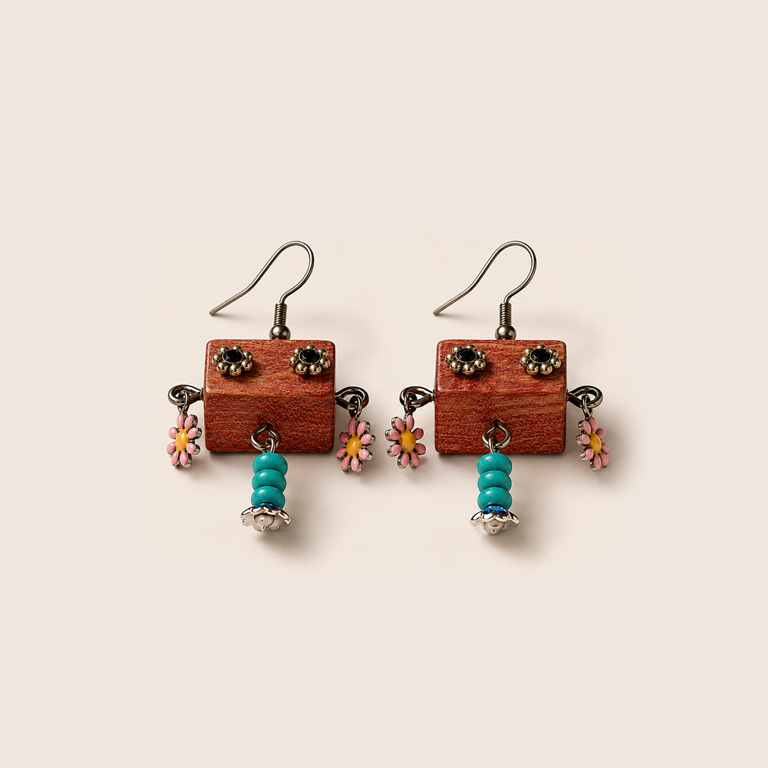 A pair of handmade dangle earrings featuring rectangular reddish-brown wooden blocks with metal ear hooks, small dark metal studs, pink and yellow flower charms, and turquoise bead drops, shown on a light beige background.