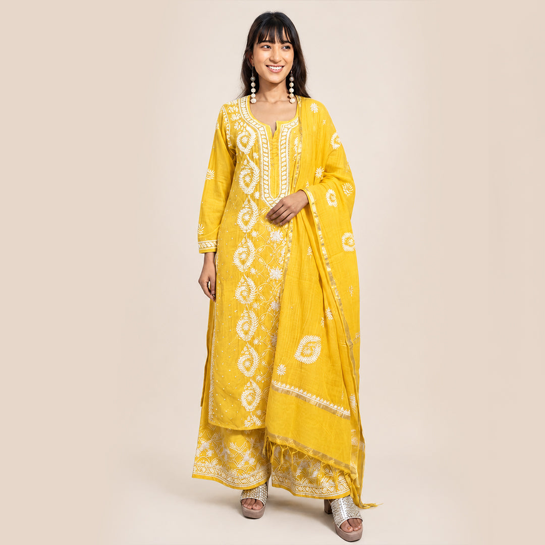 A woman modeling a bright yellow Indian ethnic suit with white printed patterns and a matching dupatta, set against a solid beige studio background.