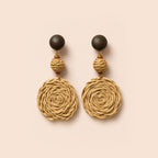 A pair of bohemian dangle earrings featuring large natural jute rope spiral discs, a small wrapped bead, and dark brown wooden sphere studs, displayed on a solid pale peach background.