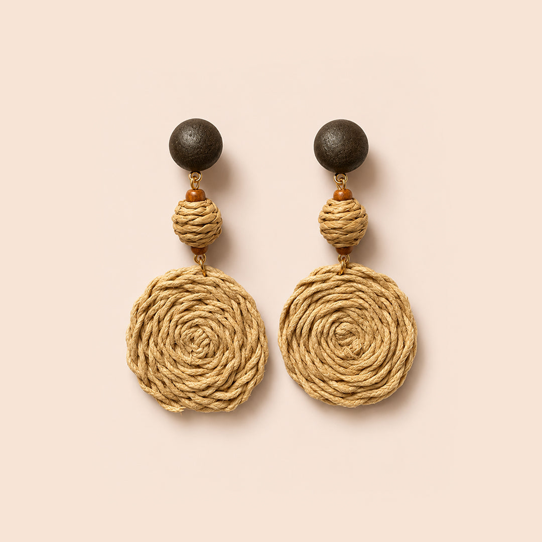 A pair of bohemian dangle earrings featuring large natural jute rope spiral discs, a small wrapped bead, and dark brown wooden sphere studs, displayed on a solid pale peach background.