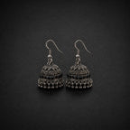 A pair of silver-toned filigree jhumka earrings with small black bead accents, displayed on a dark textured background.