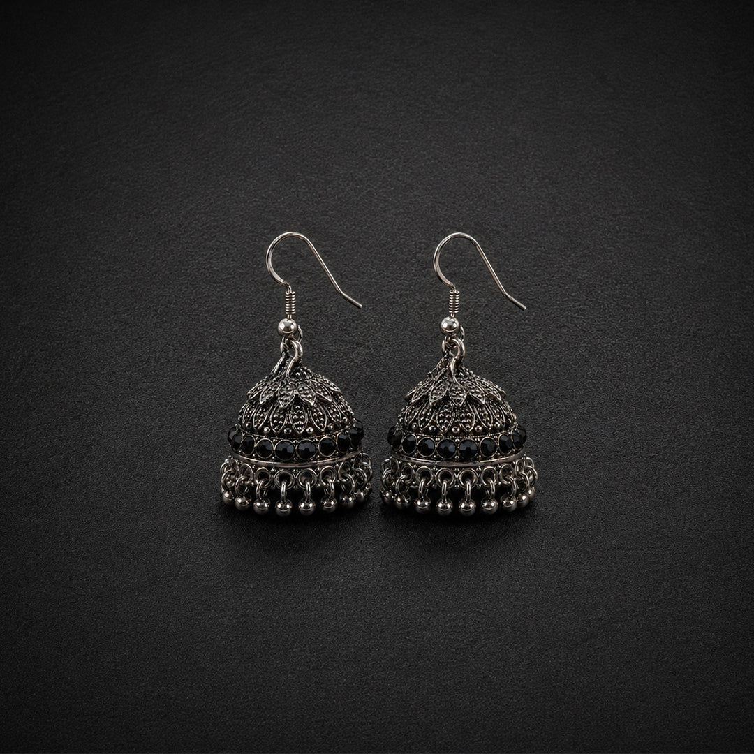A pair of silver-toned filigree jhumka earrings with small black bead accents, displayed on a dark textured background.