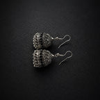 A pair of silver-toned filigree jhumka earrings with hook backs, displayed on a textured black background.