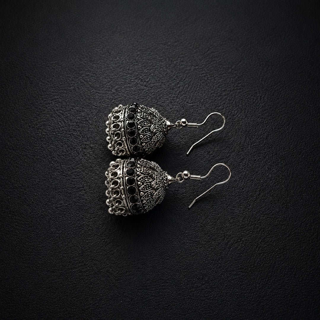 A pair of silver-toned filigree jhumka earrings with hook backs, displayed on a textured black background.