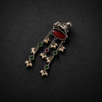 A silver-toned traditional Indian pendant featuring a horse motif, an oval red cabochon stone, and three dangling chains with green and red stones and pearl-like beads, displayed on a dark textured background.